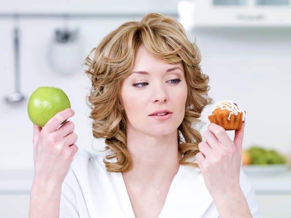 Young beautiful woman choose between sweet cake and green apple - in the kitchen