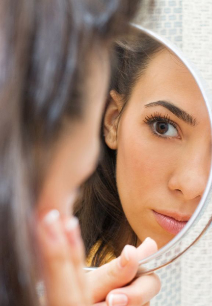 Young woman looking  at her face  in the mirror